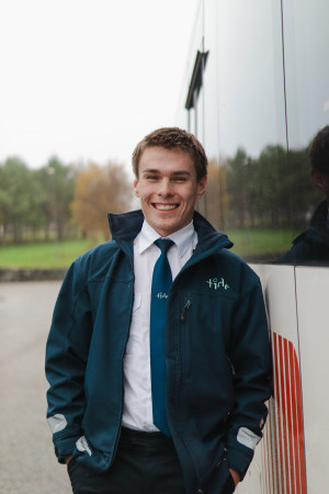 Ung bussjåfør som smiler foran en buss.