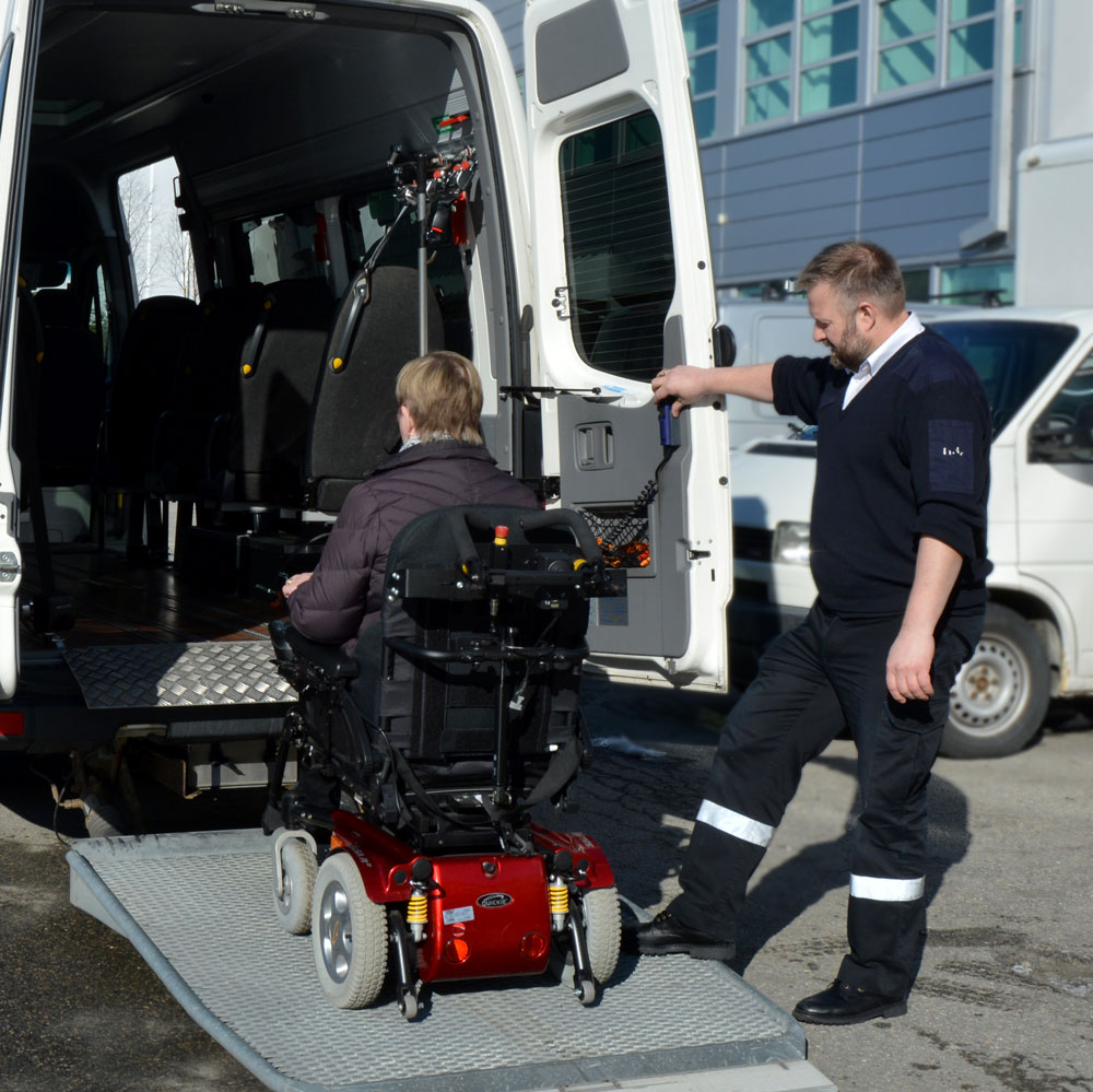 Mann som hjelper en rullestolbruker inn i en buss.